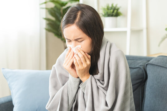 Sick, coronavirus or covid, tired asian young woman have a fever, flu and hand in use tissues paper sneezing nose, runny while sitting on sofa, couch at home. Health care with disease, pandemic virus