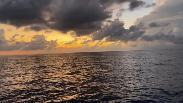 Dramatic sunset over the open ocean with contrasting golden light on one side and silvery gray clouds on the other. The camera slowly pans horizontally across the seascape, capturing warm evening ligh