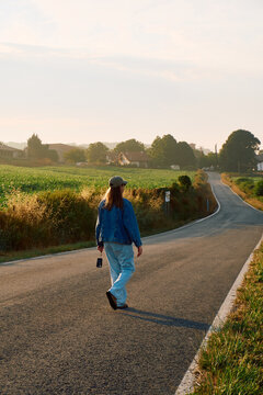 Woman in denim jacket walking down an empty country road