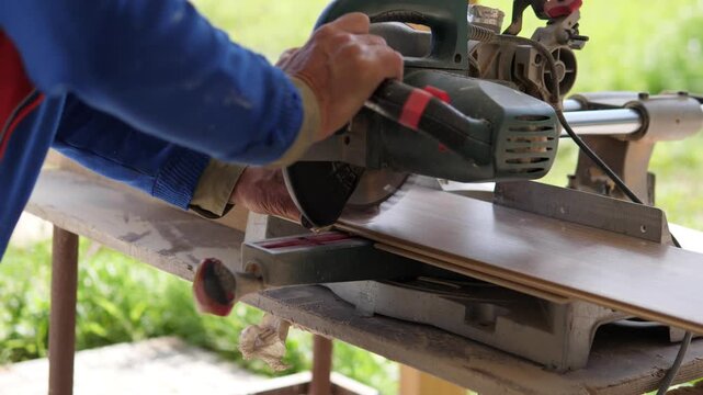 Adult hands steady handheld circular saw over clamped wooden plank on outdoor workbench, framed in tight side view with blue work jacket, metal guide, rough wood grain, natural