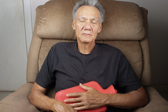 Older Man Applying a Hot Water Bottle on his stomach for pain relief  