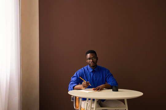 Young Man Writing at Desk in Blue Shirt