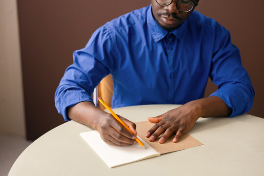 Man Writing In Notebook At Table With Pencil