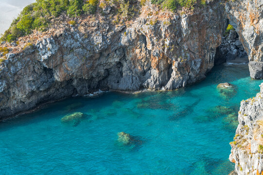 High angle view of Arcomagno sea cave and turquoise lagoon with rugged limestone cliffs in San Nicola Arcella, Calabria, Italy.