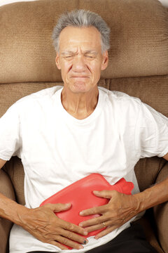 Older Man Applying a Hot Water Bottle on his stomach for pain relief  