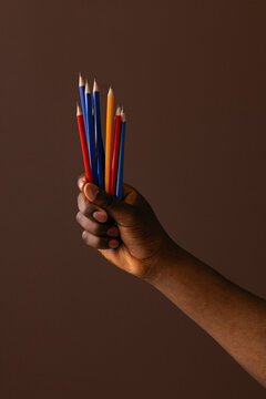 Hand Holding Colorful Pencils Against Brown Background