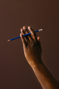 Hand Holding Blue Pencil Against Brown Background