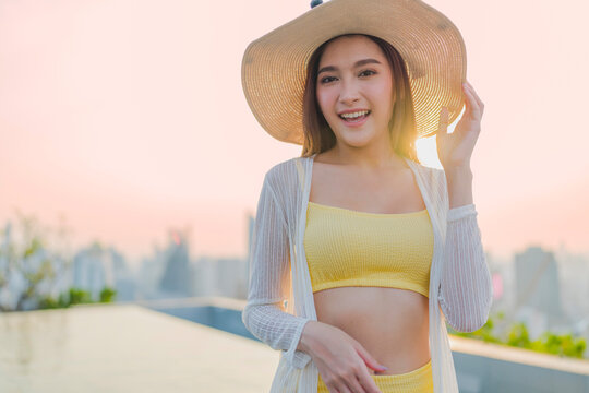 Portrait of cheerful smiling young woman wearing sun hat enjoying golden hour sunset at luxury rooftop, radiating joyful optimism, vitality, happiness, freedom, and vacation vibes.