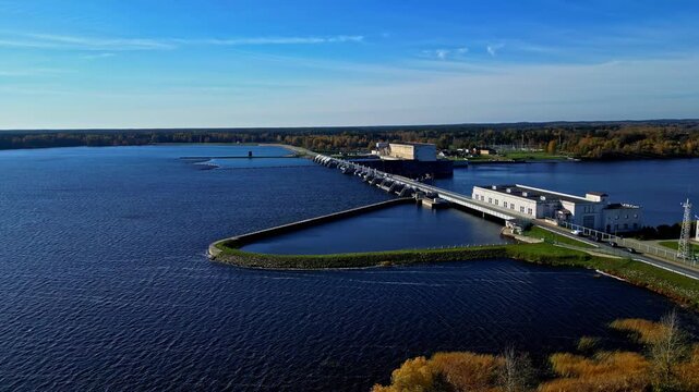 Aerial view of Kegums HES hydroelectric power plant on the Daugava River surrounded by forests under a clear blue sky in Kegums, Ogres novads, Latvia.