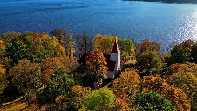 Aerial view of the historic church surrounded by vibrant autumn trees near the river in Kegums, Ogres novads, Latvia.