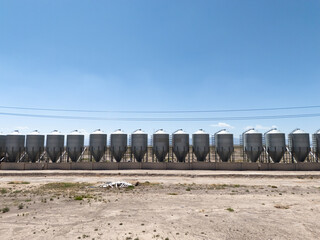 row of grey industrial grain silos under blue sky © zhu difeng