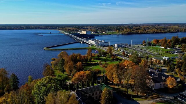 Aerial view of Kegums Hydroelectric Power Station on the Daugava River with surrounding autumn forest and clear blue sky in Kegums, Ogres novads, Latvia.
