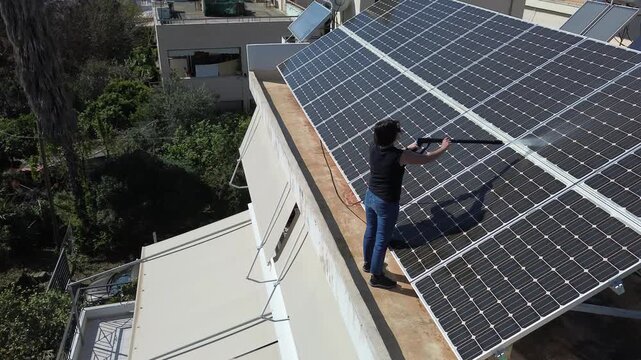 Aerial view of caucasian woman cleaning rooftop solar panels with a pressure washer