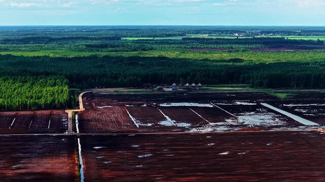 Aerial view of peat bog with dark soil and drainage channels surrounded by forest in Jelgava, Latvia.