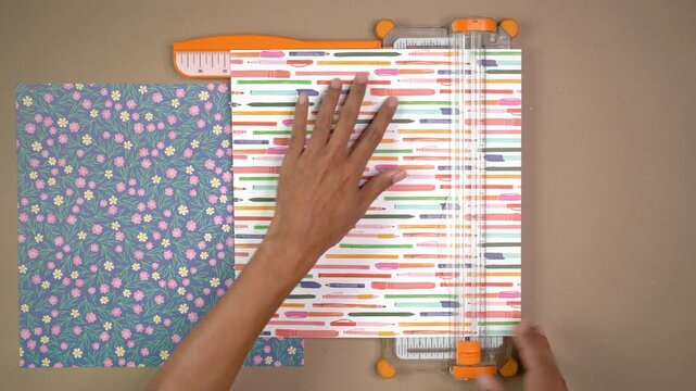 Top-down view of person's hands using guillotine to cut patterned paper for craft project