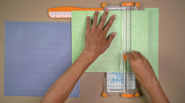 Person cutting patterned paper with trimmer for crafting project