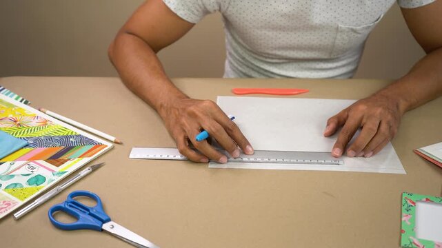 Person tracing a straight line on white sheet using ruler for craft project