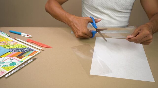 Creative male artist using scissors to cut transparent acetate sheet for handicraft project