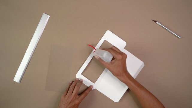 Artisan's hands applying glue to white paper to create handmade window envelope