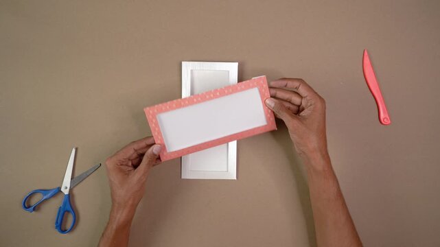 Talented man's hands folding pink polka dot paper to make handmade window envelope on desk