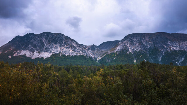 Alaska Hurricane Train wilderness travel landscape with snow dusted mountain peaks and forest on a cloudy autumn morning