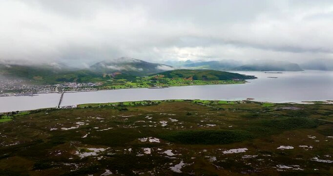 Sortland in Vesteralen, Northern Norway. Dolly view towards bridge over the water with mist-covered City landscape, Wide cinematic aerial view