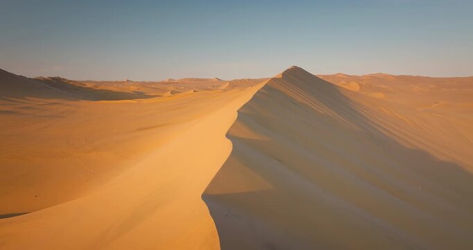 Drone view over golden sand dunes in Huacachina desert at sunset in Ica, Peru. Aerial forward