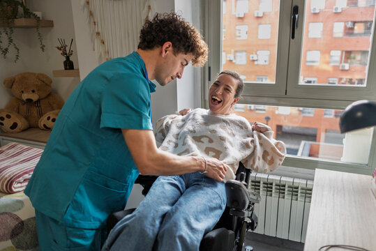 Caregiver assisting disabled woman in wheelchair laughing together