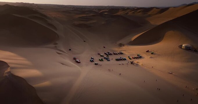 Dune buggies gathered on sand dunes in Huacachina desert in Ica, Peru. Aerial backward tilt-up reveal