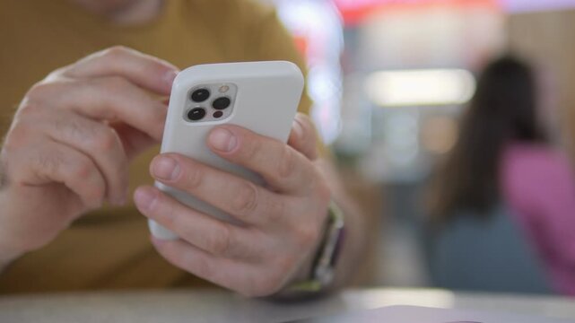 Hands scroll smartphone in casual setting. Person focused on screen, unaware of surroundings. Ideal for tech, communication, or daily life themes. Soft focus background adds relaxed mood