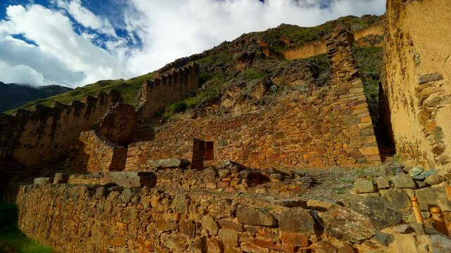 Ancient stone and adobe ruins rise on a rugged hillside in Ollantaytambo, Sacred Valley, Peru, establishing medium pan left at golden sunset light