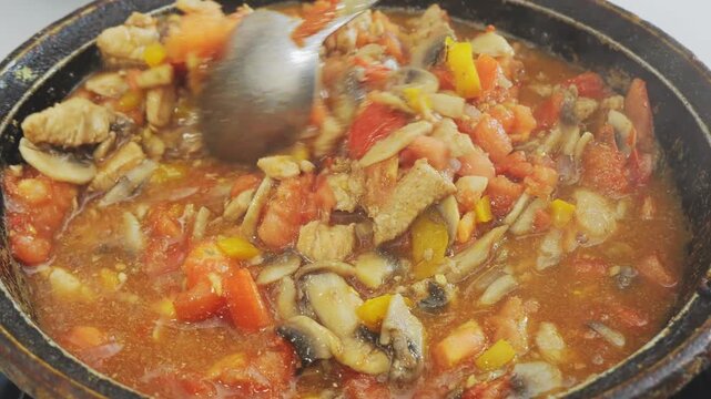 Chicken with vegetables in a sauce and spices is stewed in a deep cast-iron skillet. Medium shot.