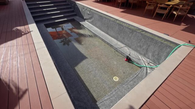 A top view captures a rooftop pool with a small drainage hose near the steps surrounded by a wooden deck