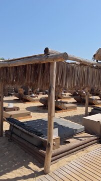 Rustic wooden beach cabana with a thatched palm leaf roof and comfortable daybed on sandy shore under clear sky