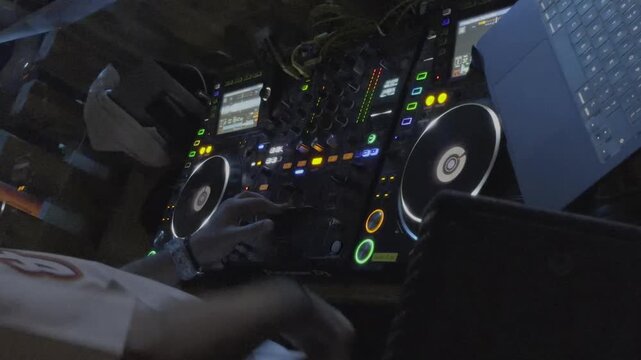 A wide angle shot shows a full DJ controller with dual turntable jog wheels and a laptop under blue tinted lighting