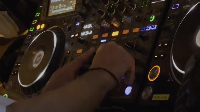 A close up view shows a hand pressing colorful illuminated buttons on professional DJ turntable decks