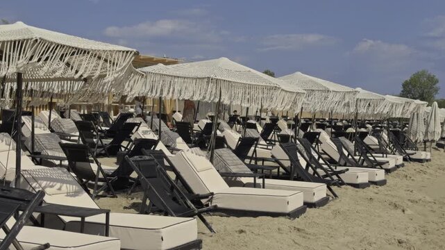 Wide view of many rows of empty sun loungers and fringed umbrellas set up on the sand at a beach club in Chalkidiki Greece