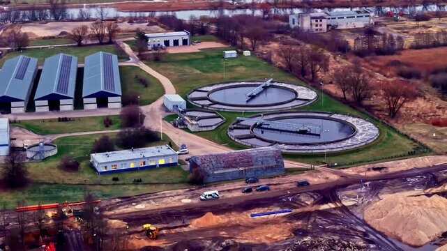 Aerial view of the wastewater treatment plant featuring circular sedimentation tanks, industrial buildings, and surrounding infrastructure in Jelgava, Latvia.