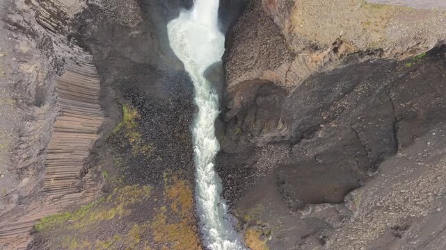 Top down aerial view of the powerful Litlanesfoss waterfall cascading through a rocky canyon framed by unique hexagonal basalt columns in Iceland