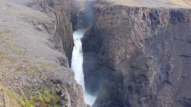 Powerful Litlanesfoss waterfall thundering down a steep canyon surrounded by spectacular hexagonal basalt columns in East Iceland