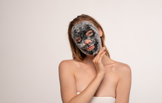 Woman applying detoxifying bubble sheet mask for healthy skin, receiving a facial treatment