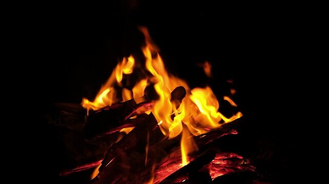 Warm flickering firelight from a burning campfire at night. A nighttime fire produces a soft, warm glow as flames flicker between burning wooden logs. The continuously moving flames and glowing embers