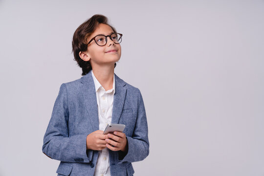 10s smart boy dreaming in formal attire holding mobile phone isolated on grey background, childhood, technology, future businessman, communication, imagination and career concept