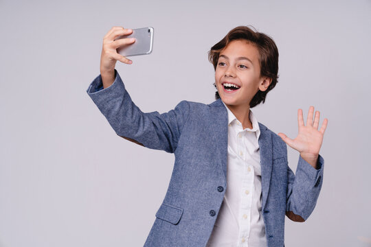 Playful young boy having a video call on his phone isolated on grey background, childhood, technology, communication, online chatting and lifestyle concept
