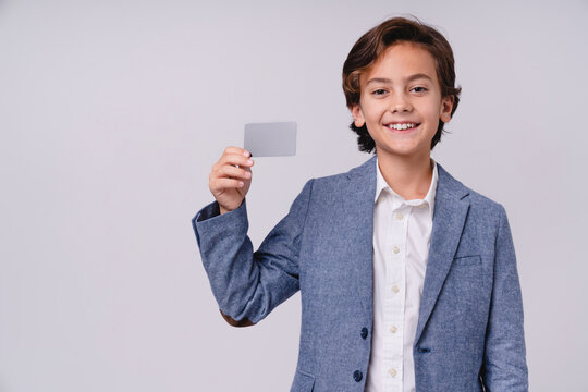 Cheerful small male kid holding credit card in formal outfit isolated on grey background, childhood, finance, payment, shopping, future businessman, success and money concept