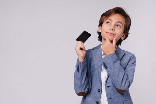 Thoughtful young boy with credit card in formal attire isolated on grey background, childhood, finance, payment, shopping, future businessman, money and lifestyle concept
