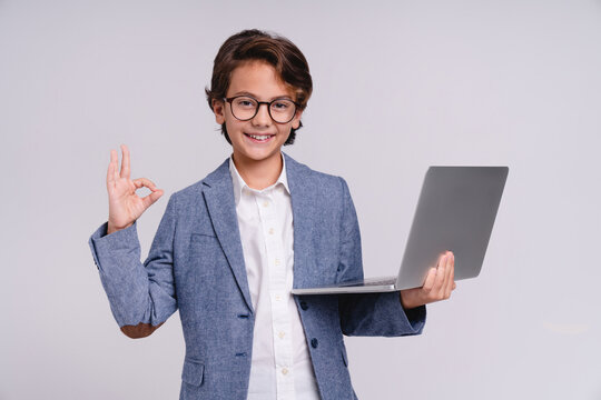 Little boy holding a laptop in formal clothes showing okay sign isolated on grey background, childhood, technology, education, future businessman, digital learning, success and professional concept