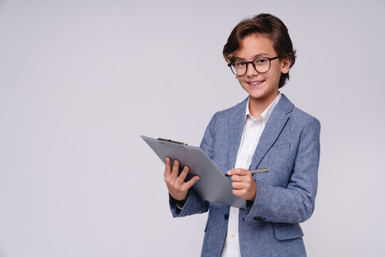 Successful small male kid in formal attire writing on clipboard isolated on grey background, childhood, future businessman, education, career, leadership and professional concept