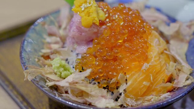 Close-up of a premium donburi bowl topped with assorted sashimi, creamy uni, and vibrant salmon roe over steamed sushi rice, beautifully arranged for an elegant Japanese meal.