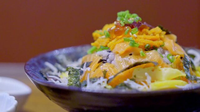 Close-up of a premium donburi bowl topped with assorted sashimi, creamy uni, and vibrant salmon roe over steamed sushi rice, beautifully arranged for an elegant Japanese meal.